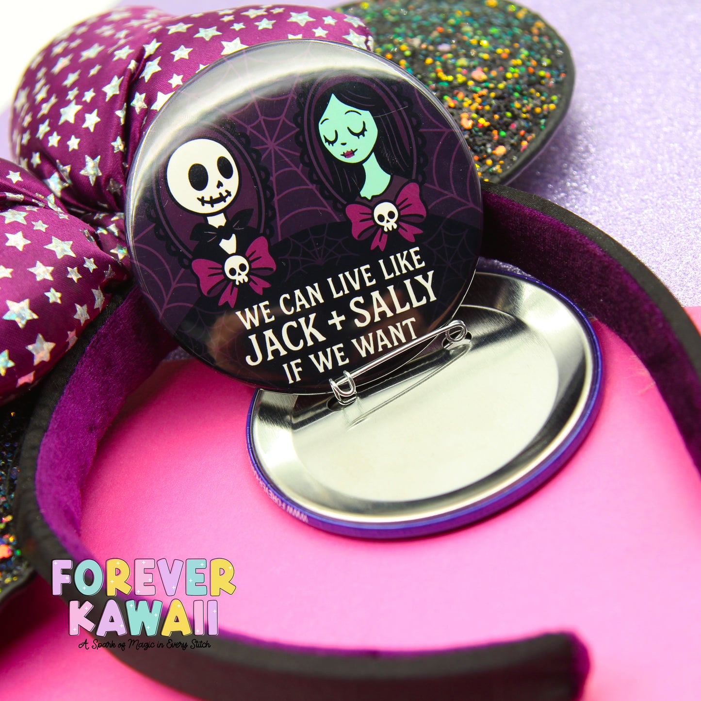 A pin with a cartoon character and text, placed on a pink surface with a purple and green glittery background.