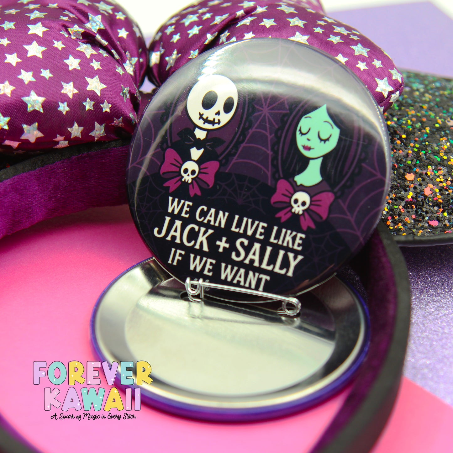A round pin with a cartoon character design and text, placed on a pink surface next to a purple and white striped fabric.