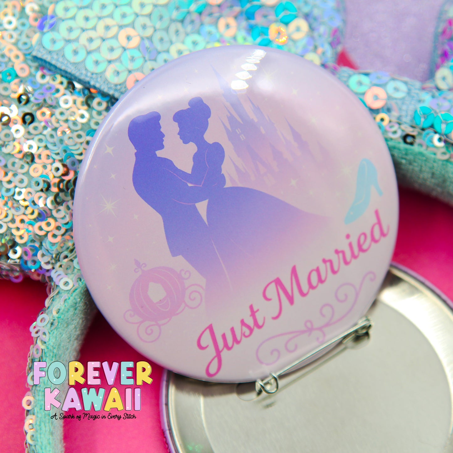 A round pin with a silhouette of a couple embracing, along with the text "Just Married" and a castle in the background. The pin is placed on a pink surface, surrounded by sequins and other decorative elements.