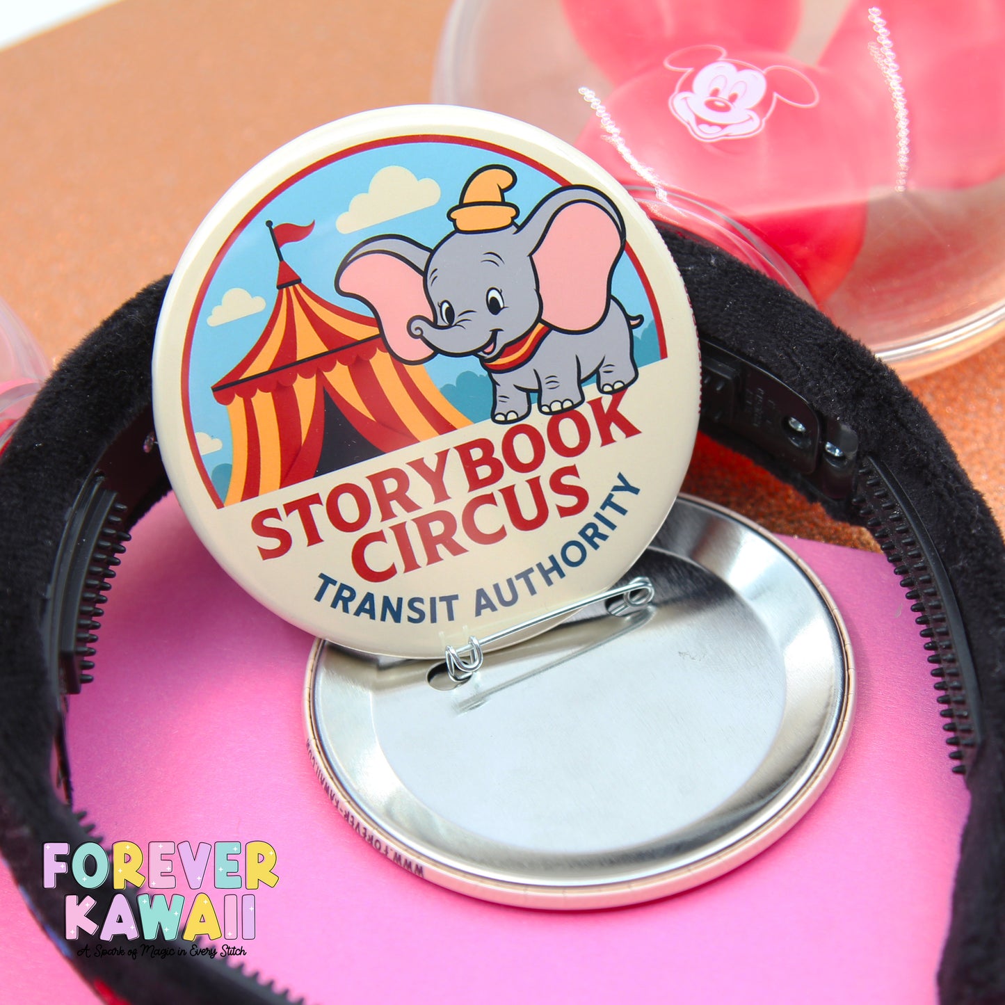 a round pin with a cartoon elephant and a circus tent, along with a black hairband.
