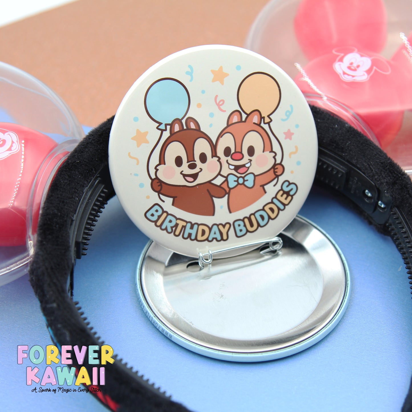 A round pin with a cartoon chip and two balloons, labeled "Birthday Buddies", is placed on a blue surface.