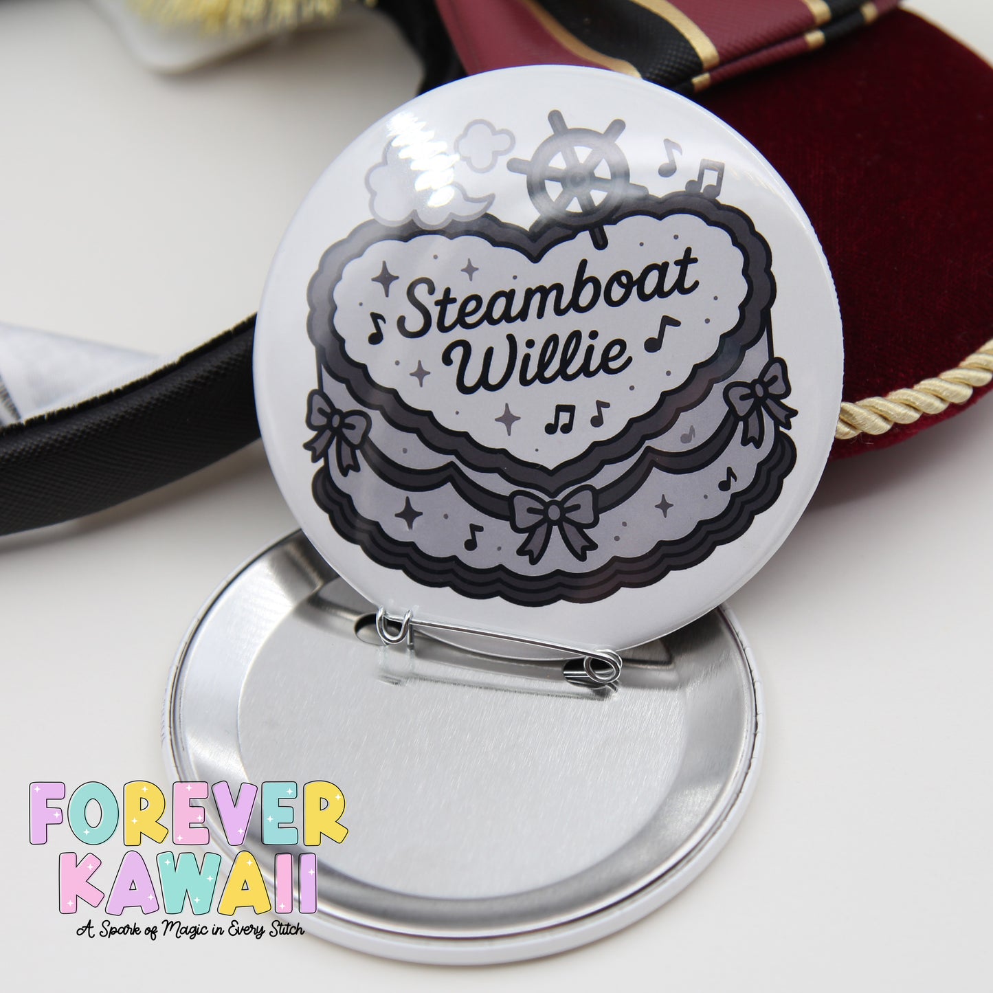 A round pin with a decorative design, featuring the text "Steamboat Willie" and musical notes, is shown on a silver surface.