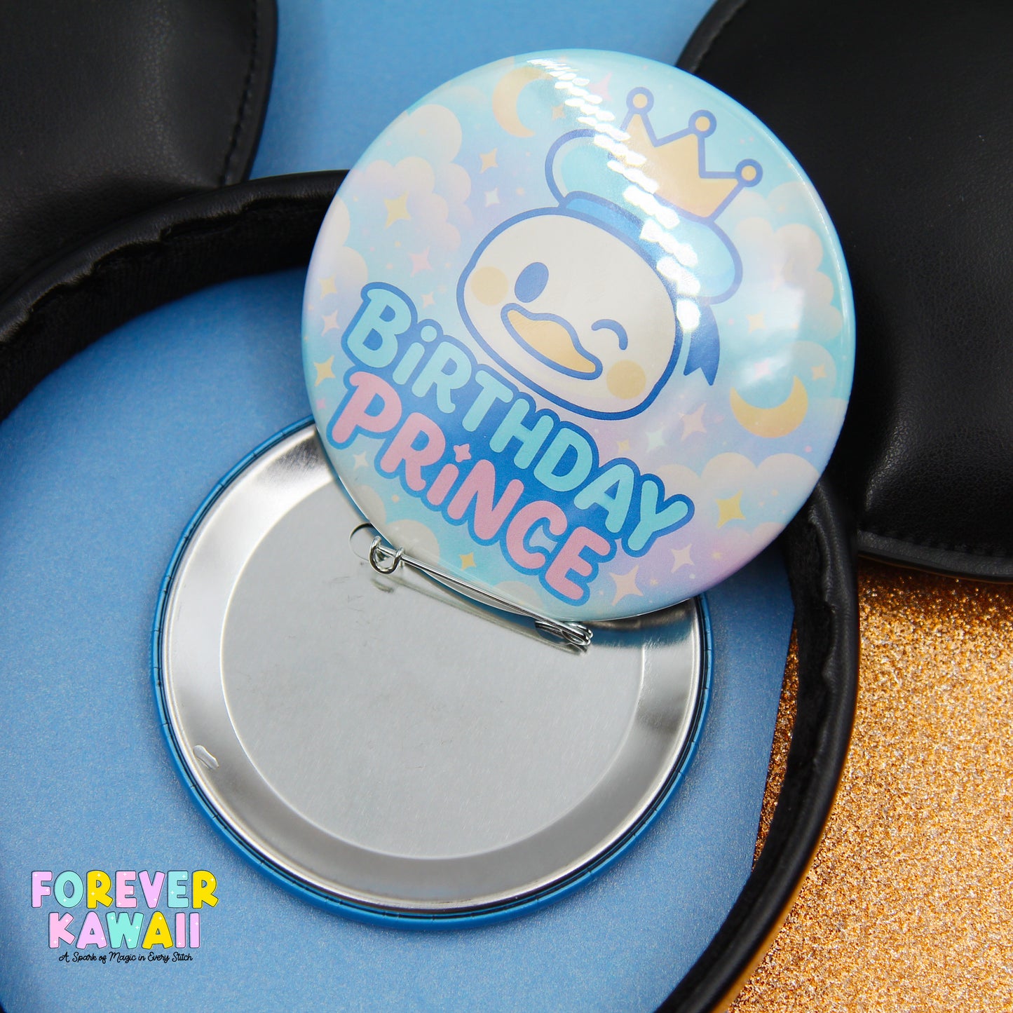 A round pin badge with a cartoon duck wearing a crown, and the text "Birthday Prince" on it, placed on a blue surface.