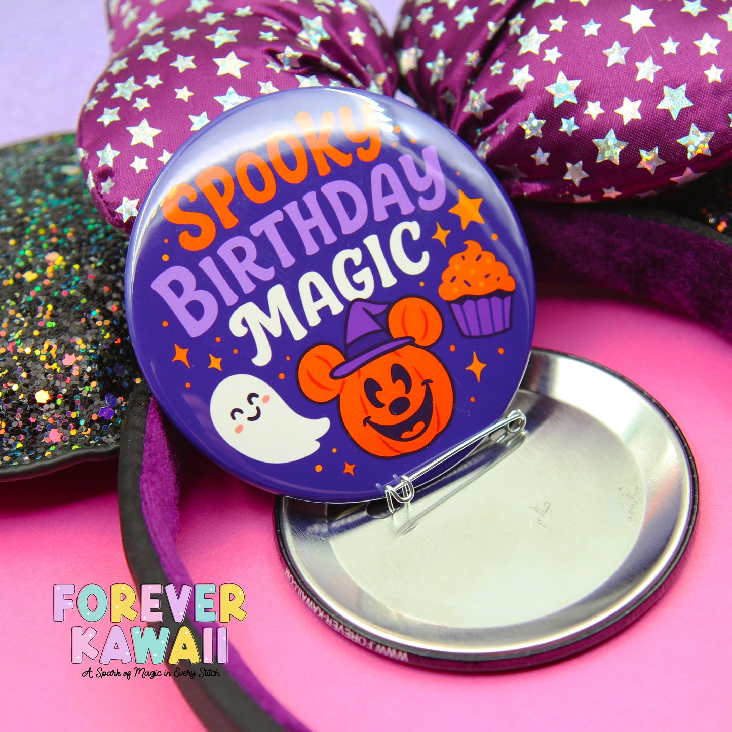 A purple button with a spooky birthday magic theme, featuring a ghost, a pumpkin, and a cupcake, is displayed on a pink surface.