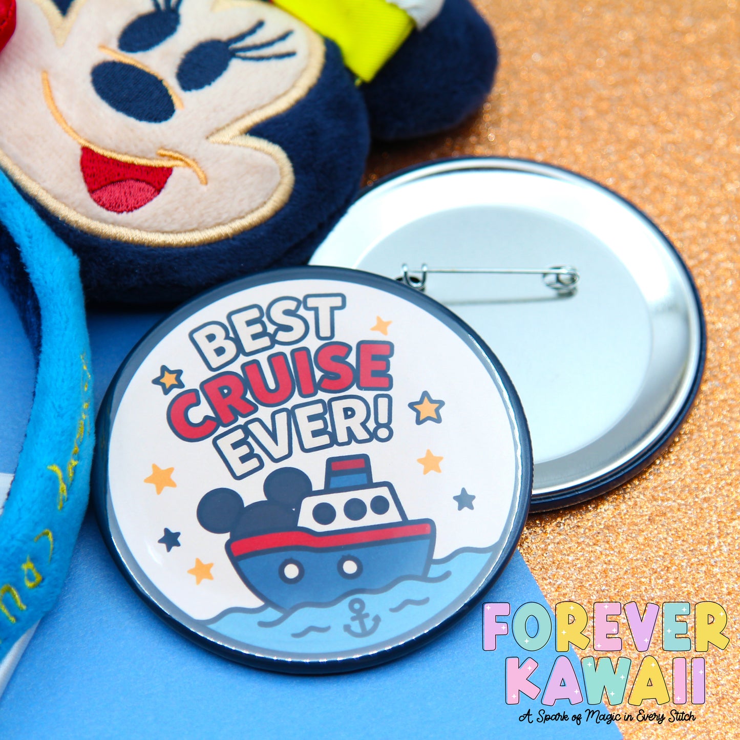 a round pin with a cartoon boat and the text "BEST CRUISE EVER!" along with a star-studded background. The pin is placed next to a stuffed animal and a silver pinback.
