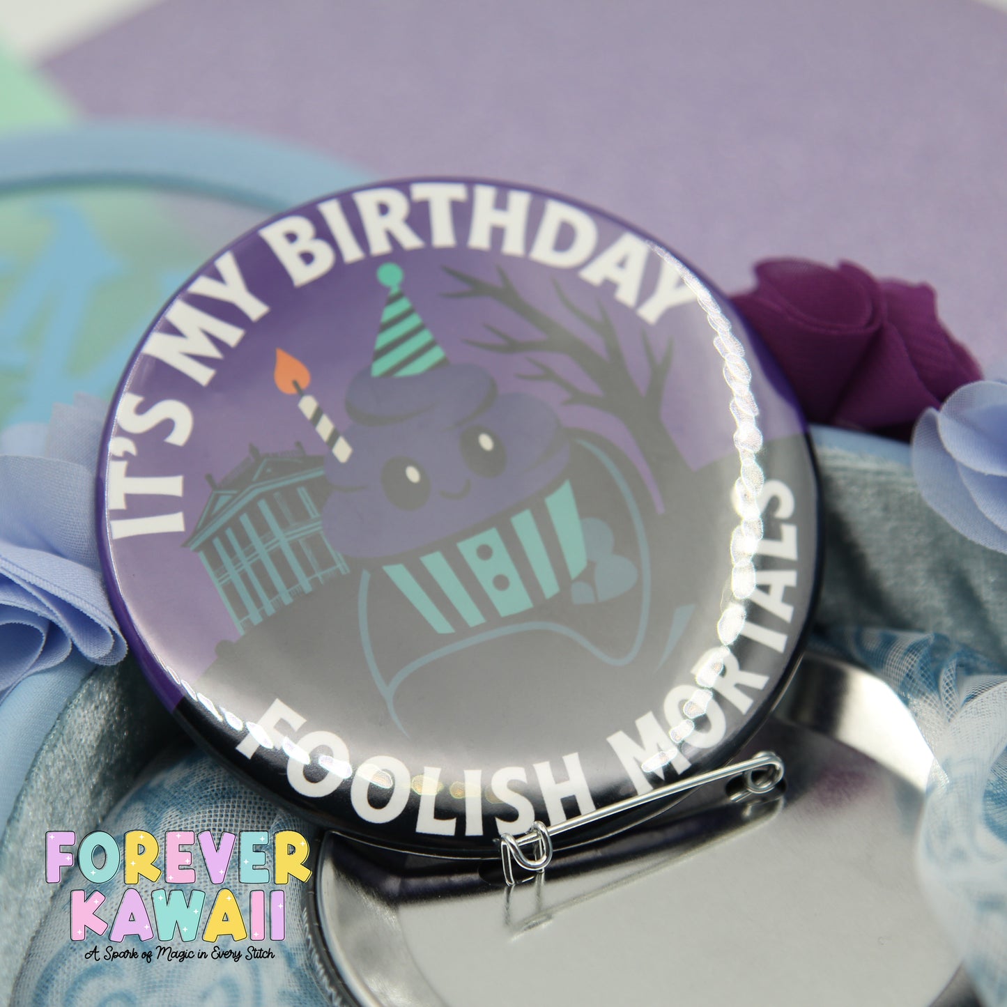 A purple button with a cartoon character and text, placed on a surface with a purple flower and a blue ribbon.