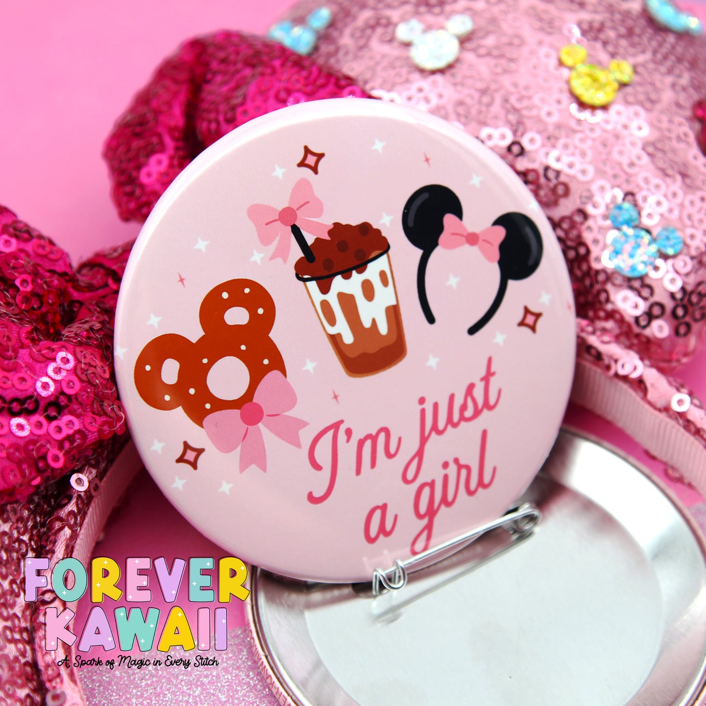 A pink pin with a playful design featuring a cupcake, Mickey Mouse ears, and the text "I'm just a girl" is displayed against a pink sequined background.