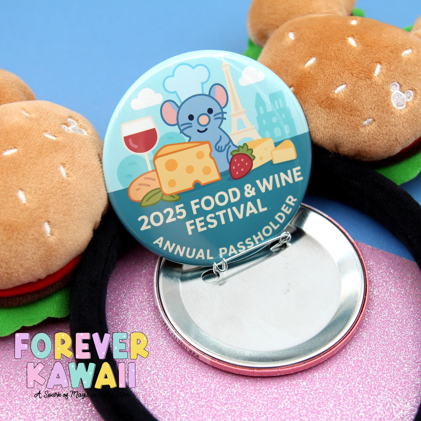 A round pin with a cartoon mouse and various food items, including a hamburger, is placed on a pink surface.