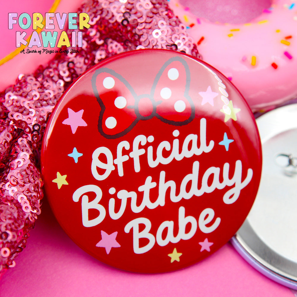 A red pin with the text "Official Birthday Babe" and a bow on it, surrounded by pink sequins and a pink donut with sprinkles.