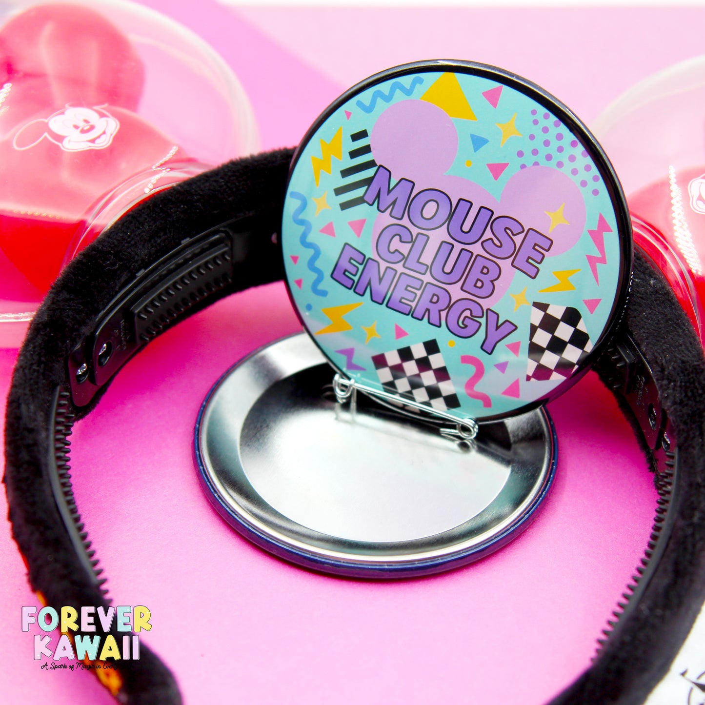 A close-up of a black headband with a colorful, circular badge featuring the text "MOUSE CLUB ENERGY" on a pink background.