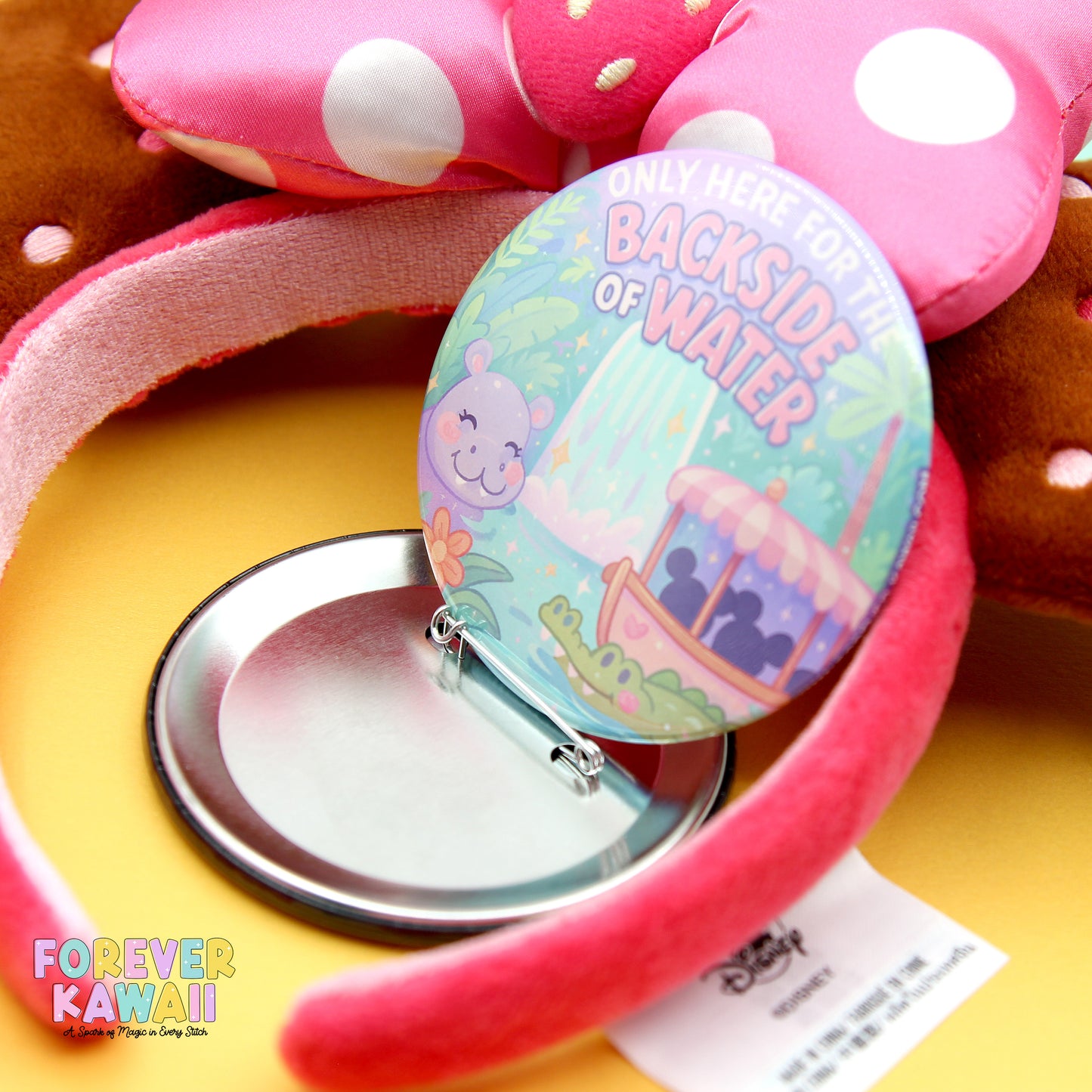 a pink and white polka dot headband with a round badge attached to it, placed on a yellow surface.