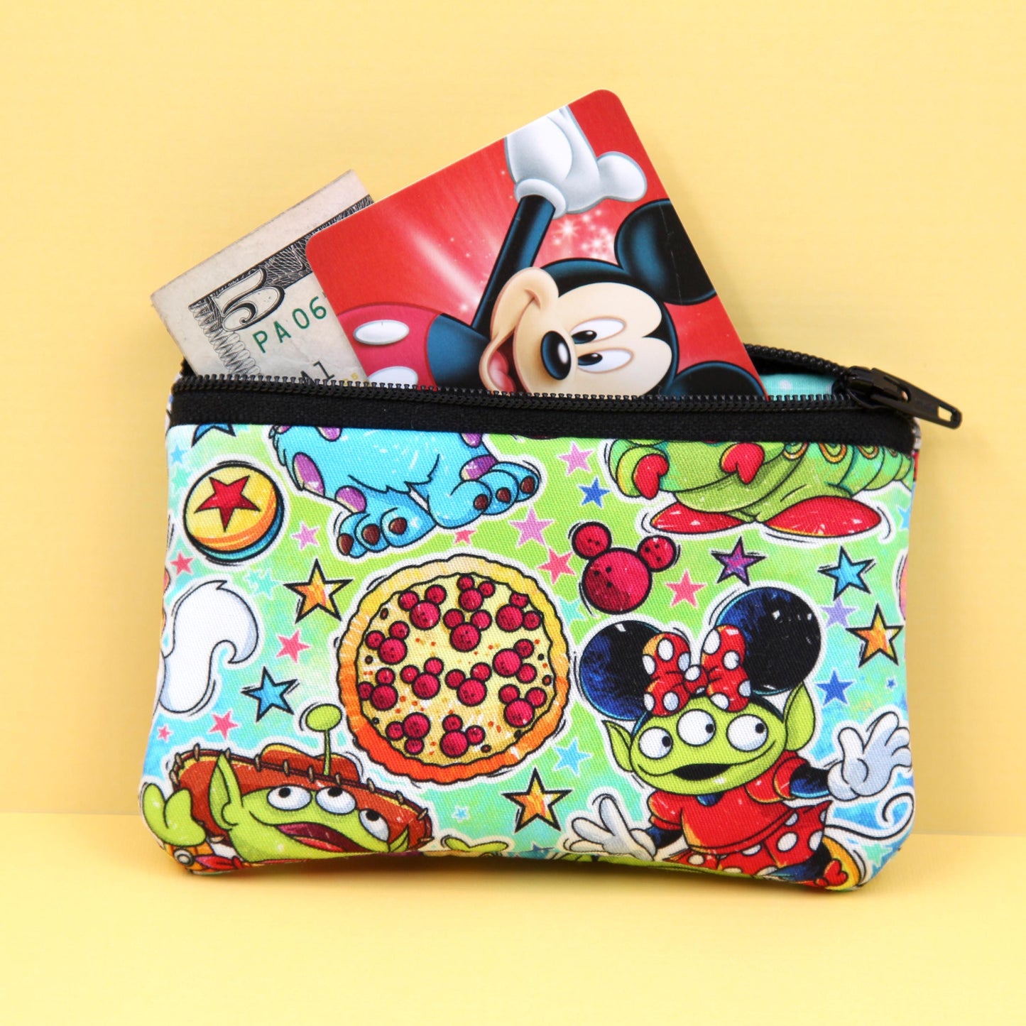 Handmade zipper pouch featuring a little green alien-inspired character dressed as various iconic Disney theme park characters, perfect for holding small essentials like coins, cards, and cash.