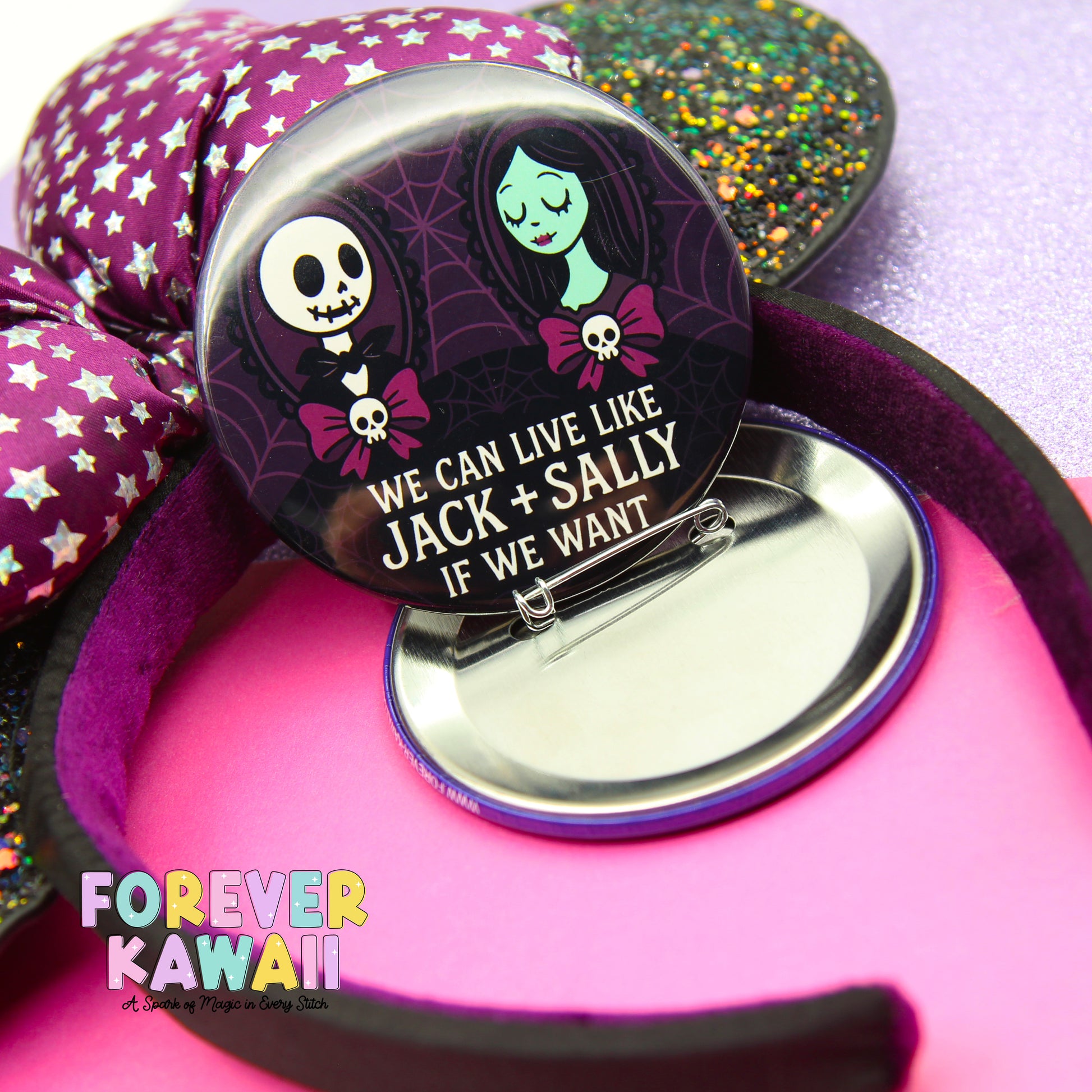 A pin with a cartoon character and text, placed on a pink surface with a purple and green glittery background.