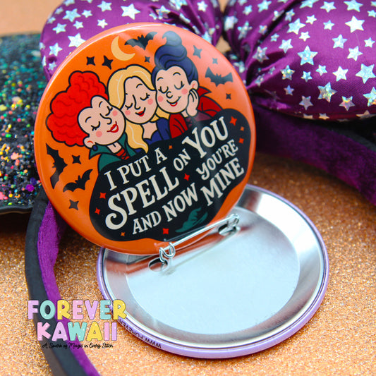a round pin with a cartoon illustration of three girls and a text message that reads "I put a spell on you and now you're mine".