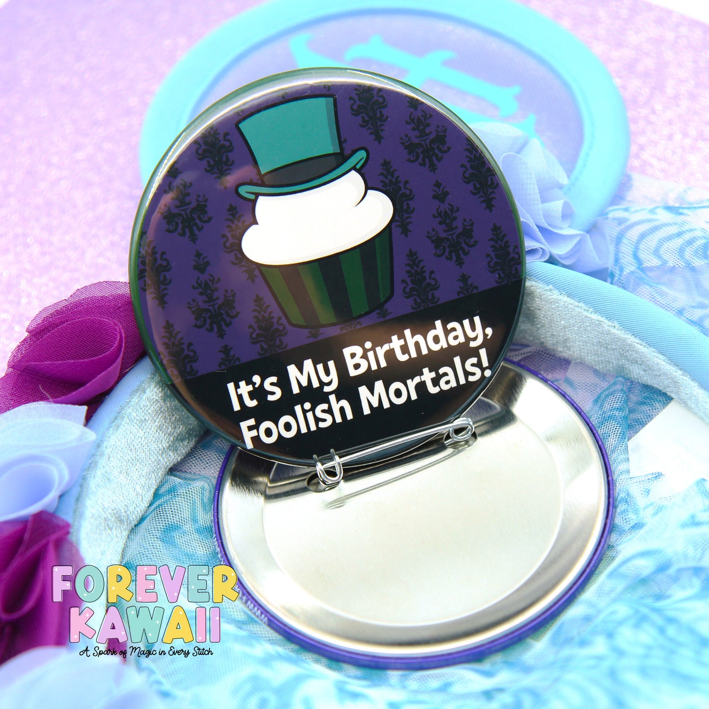 A round pin with a cartoon cupcake on it, surrounded by a purple and black pattern, and a humorous birthday message.