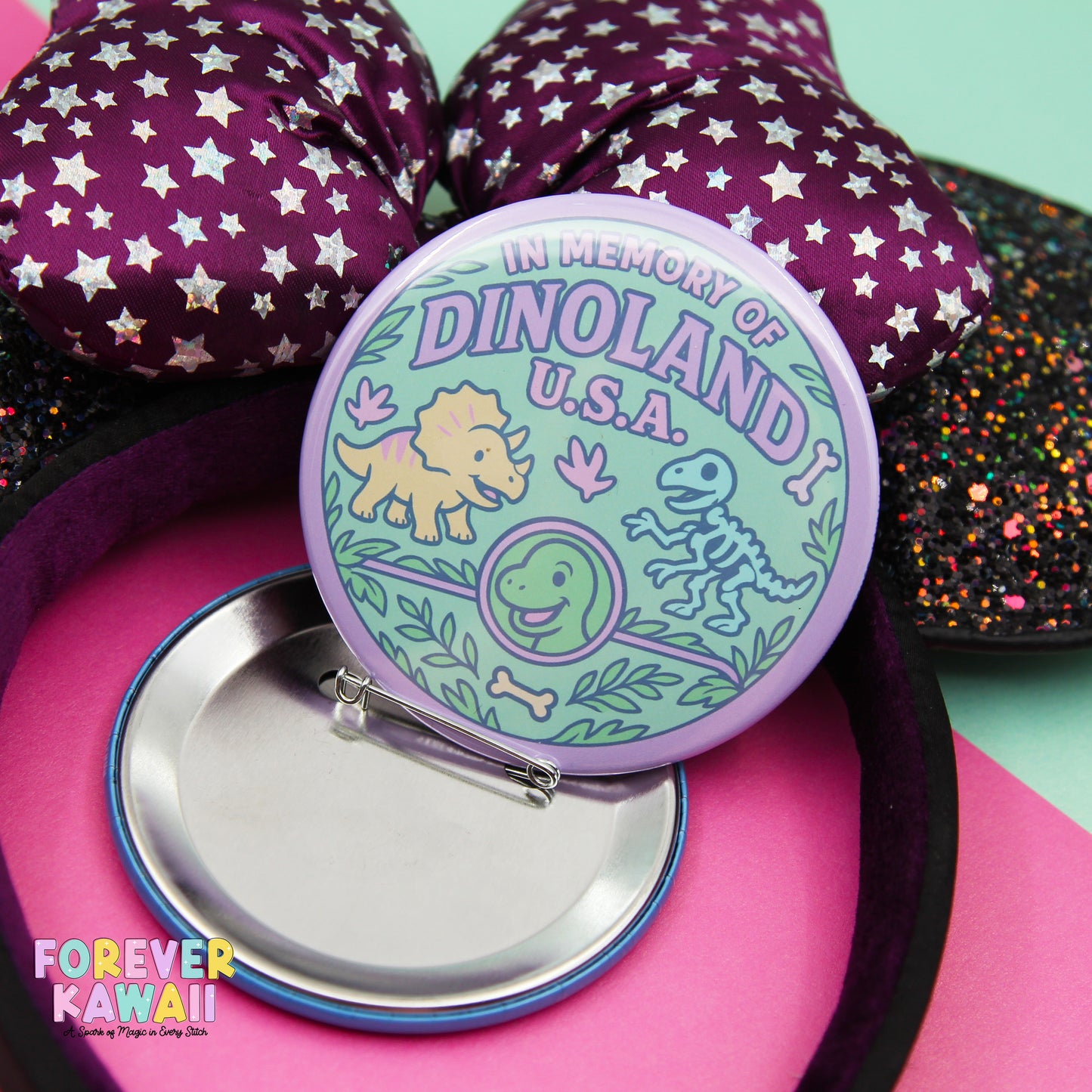 a round pin with a purple and green design, featuring a dinosaur and a triceratops, placed on a pink surface.