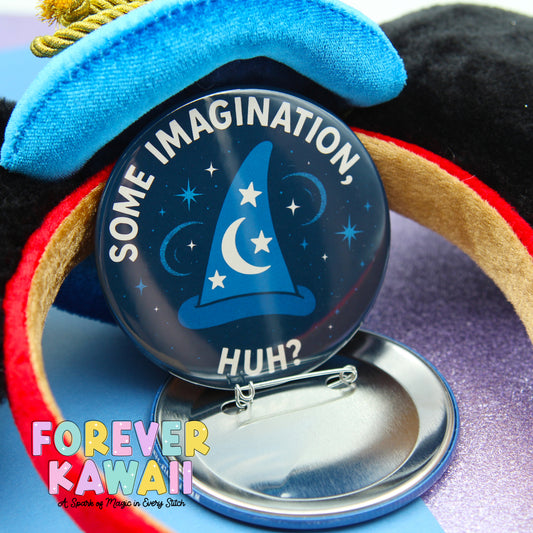 A round pin with a blue background and a white wizard hat with a crescent moon and stars, along with the text "SOME IMAGINATION, HUGH?"