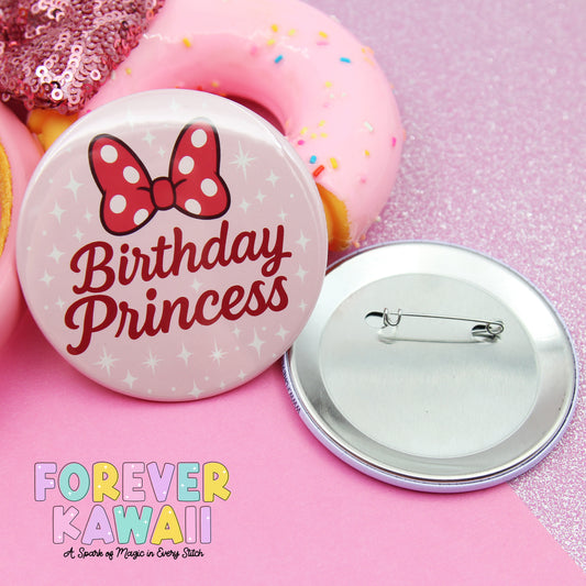 a pink birthday princess pin and a pink donut with sprinkles, both placed on a pink glittery surface.