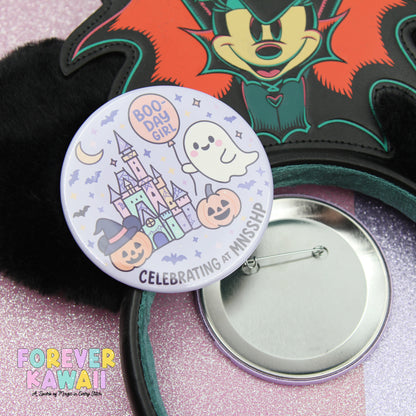a round pin with a cartoon character and Halloween-themed decorations, such as a ghost, castle, and pumpkins, along with the text "BOO-DAY GIRL" and "CELEBRATING AT MISSISSIPPI".