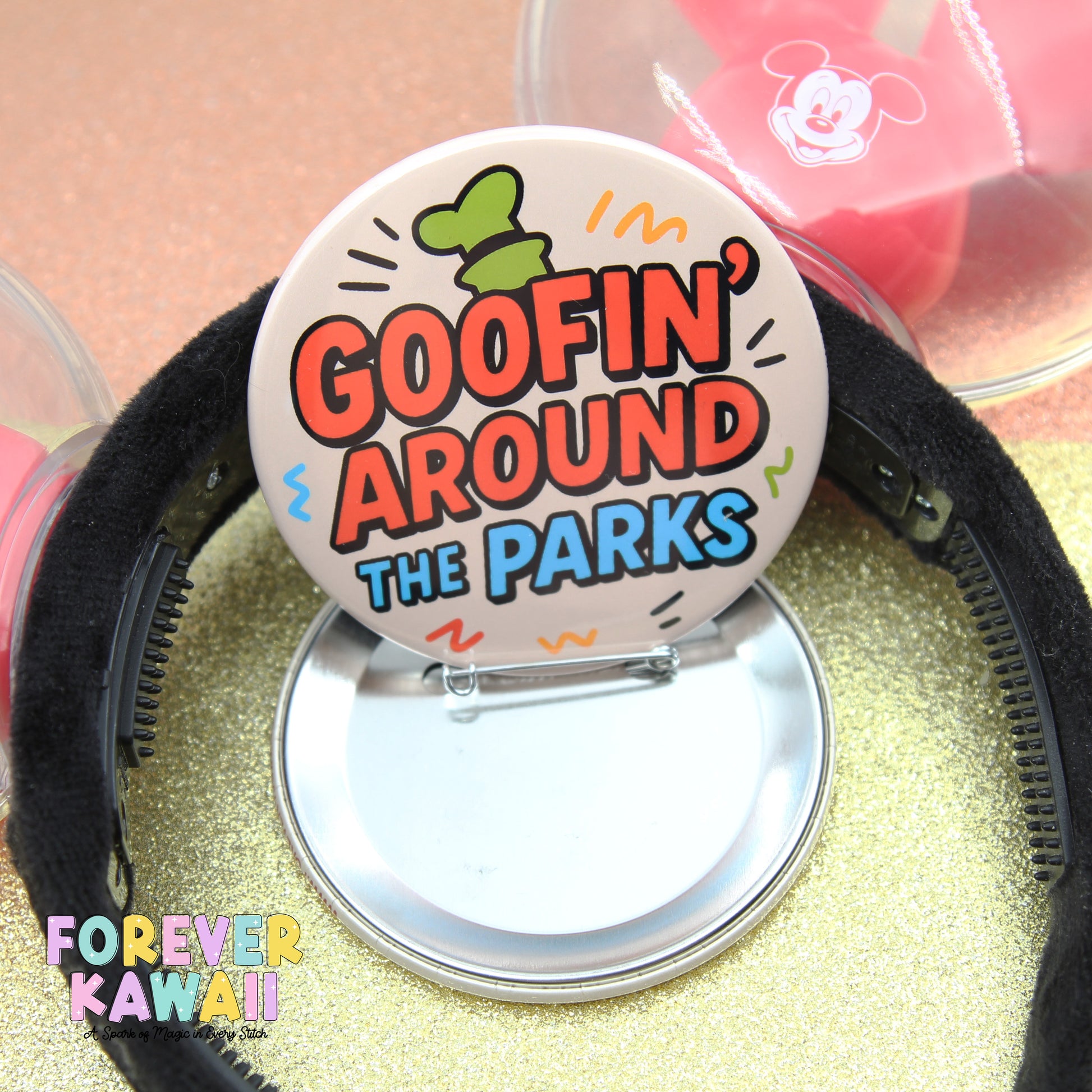 a round pin with the text "GOOFIN' AROUND THE PARKS" on it, placed on a glittery surface.