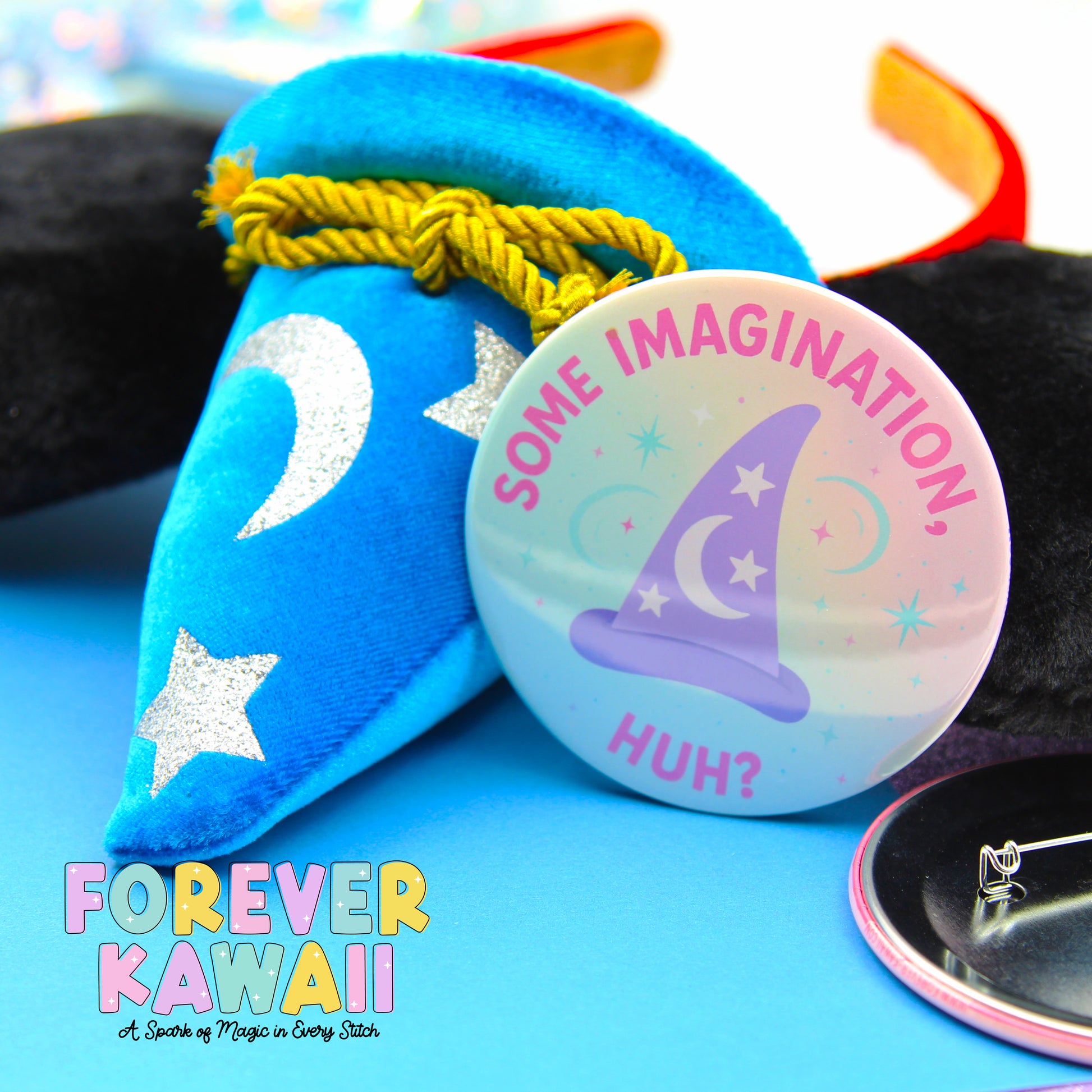 a blue wizard hat with a silver crescent moon and star, a round pin with a purple wizard hat and stars, and a black button with the text "SOME IMAGINATION HUGH?" written on it.