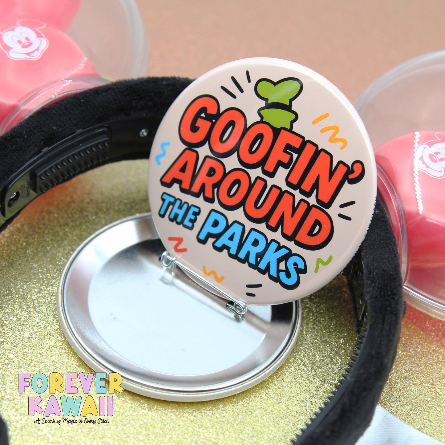 A close-up of a circular button with the text "GOOFIN' AROUND THE PARKS" printed on it, placed on a glittery surface.