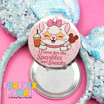 A button featuring a cartoon cat with a bow and a drink, along with the text "I Came for the Sparkles and Snacks" and the Disney character Mickey Mouse. The button is placed on a pink background, and there is a bow and a drink visible in the image.