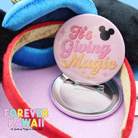 a pink pin with the text "It's Giving Magic" and a black Mickey Mouse symbol, along with a red ribbon and a blue hat.