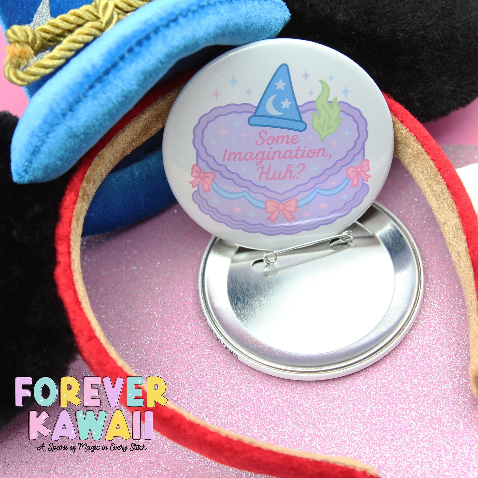 A round pin with a blue hat and a red headband is placed on a pink glittery surface.