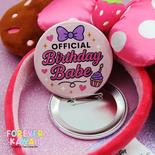 a pink birthday bib with a bow and the text "OFFICIAL BIRTHDAY BABE" printed on it, placed on a pink background. There is also a pink stuffed animal and a pink headband visible in the image.