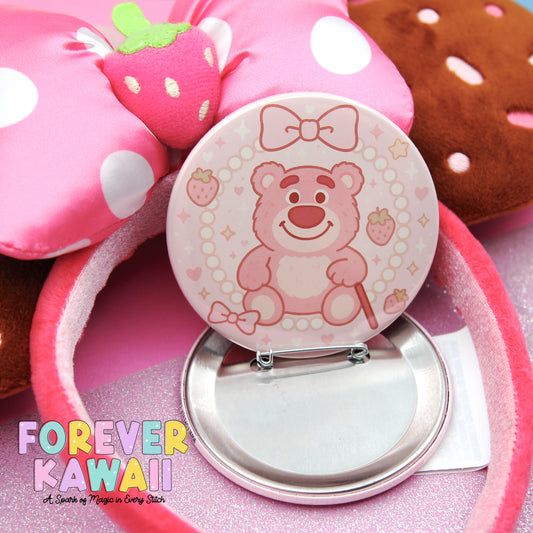 A pink pin with a cartoon bear design and a bow on a pink background, surrounded by other pink and white polka dot items.