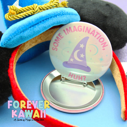 A round pin with a wizard hat and the text "Some Imagination. Huh?" is placed on a silver stand, surrounded by a blue background and a red ribbon.