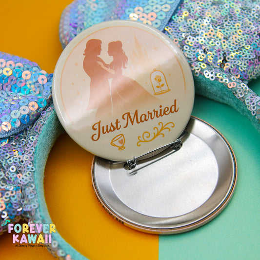 A round pin with a silhouette of a couple and the text "Just Married" on it, placed on a surface with sequin details.