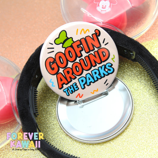a round button with the text "GOOFIN' AROUND THE PARKS" printed on it, placed on a glittery surface.